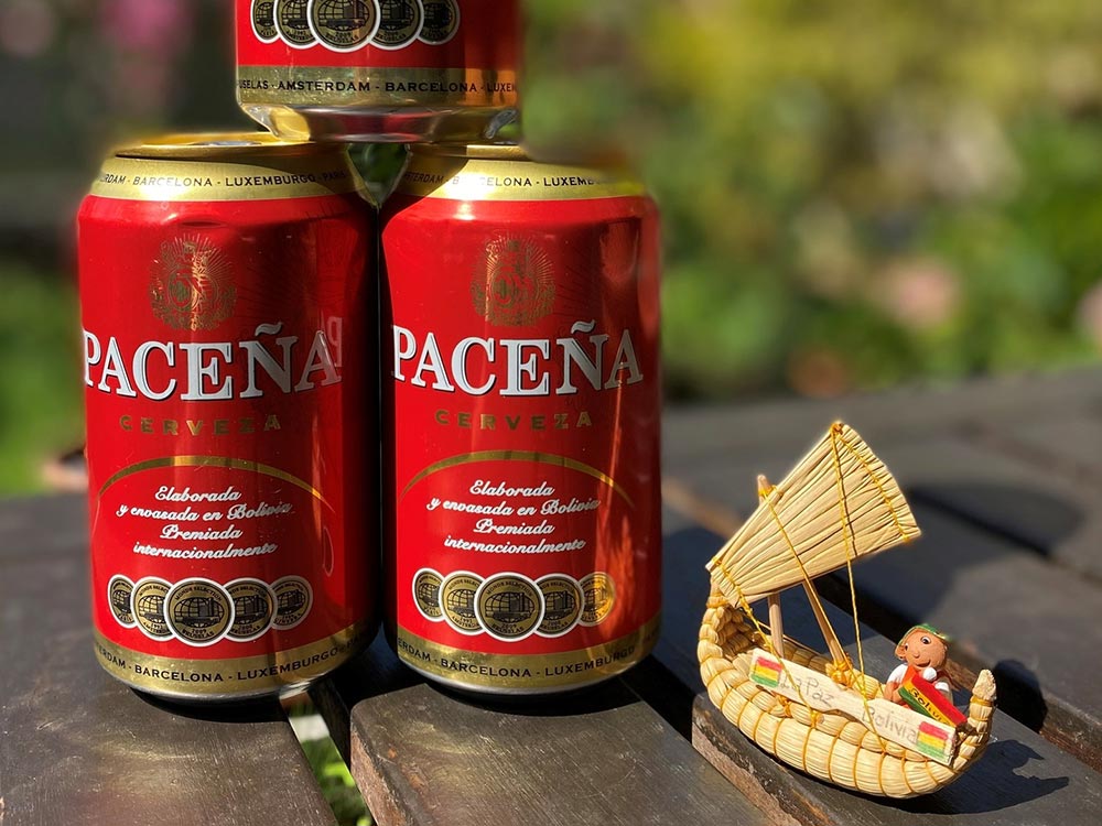 Zwei Dosen Cerveza Paceña auf einem Tisch im freien, rechts daneben ein kleines bolivianisches Schiffchen